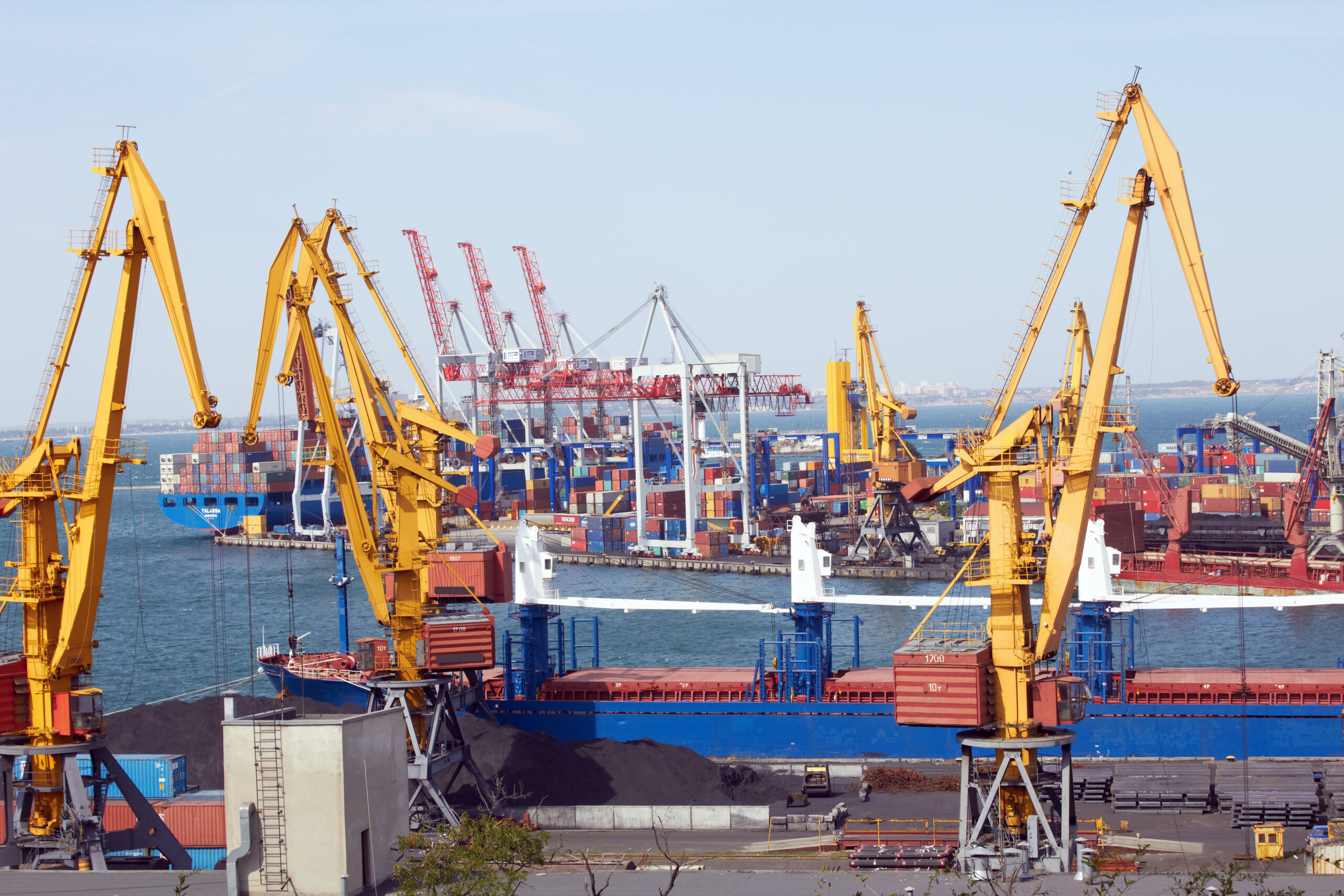 Industrial port with multiple cranes loading and unloading containers onto cargo ships docked at the terminal.